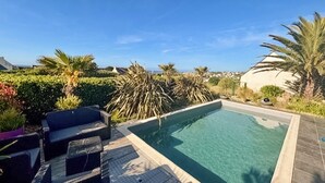 A swimming pool with a wooden deck, lounge chairs, and palm trees.
