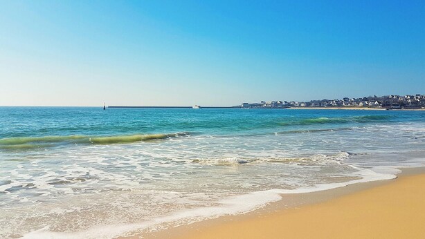 A beach with clear blue water, gentle waves, and a sandy shore.