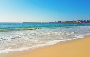 Een strand met helderblauw water, rustige golven en een zandstrand.