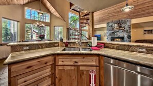 A kitchen with a granite countertop, wooden cabinets, a stainless steel sink, and a stone fireplace. - Luxury House, Hot Tub, Pet Friendly, Pool Table, EV Charger
 (South Lake Tahoe)