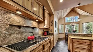A kitchen with wooden cabinets, a granite countertop, a red kettle, and a stone backsplash. - Luxury House, Hot Tub, Pet Friendly, Pool Table, EV Charger
 (South Lake Tahoe)