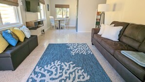 A living room with a brown sofa, a blue patterned rug, a dining table with chairs, and a TV mounted on the wall. - Downtown Villa-Fully equipped! Short drive Beaches, Short Walk to Payne Park.  (Sarasota)
