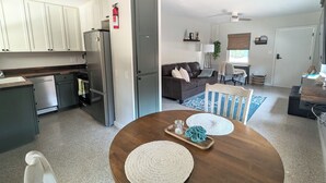 A modern kitchen with white cabinets and stainless steel appliances, a dining area with a wooden table and blue and white rugs, and a living room with a dark brown leather sofa and a TV. - Downtown Villa-Fully equipped! Short drive Beaches, Short Walk to Payne Park.  (Sarasota)