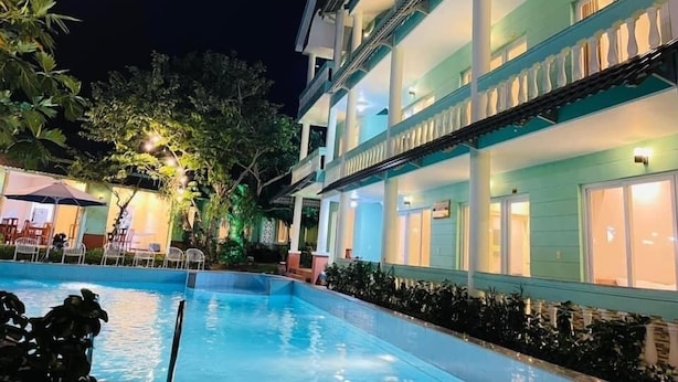 A multi-story hotel with a swimming pool, outdoor seating, and well-lit balconies. - Phú Long Bungalow (Phu Quoc)