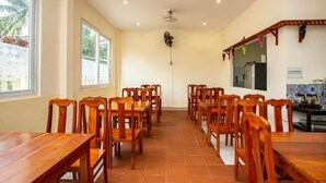 A dining area with wooden tables and chairs, a ceiling fan, and a kitchen area with a tiled backsplash. - Phú Long Bungalow (Phu Quoc)