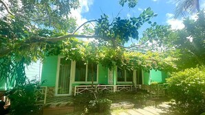 A green building with a covered outdoor seating area and a garden. - Phú Long Bungalow (Phu Quoc)