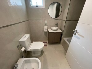 Ein kleines Badezimmer mit Toilette, Bidet, Waschbecken und einem kleinen Fenster.