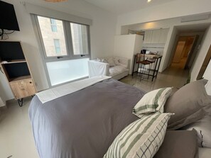 Ein modernes Schlafzimmer mit einem großen Bett, einer kleinen Couch, einem Schreibtisch und Blick ins Freie.