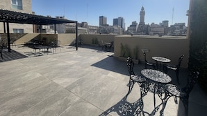 Eine Dachterrasse mit Sitzgelegenheiten im Freien, einer Pergola und Blick auf die Stadtlandschaft.