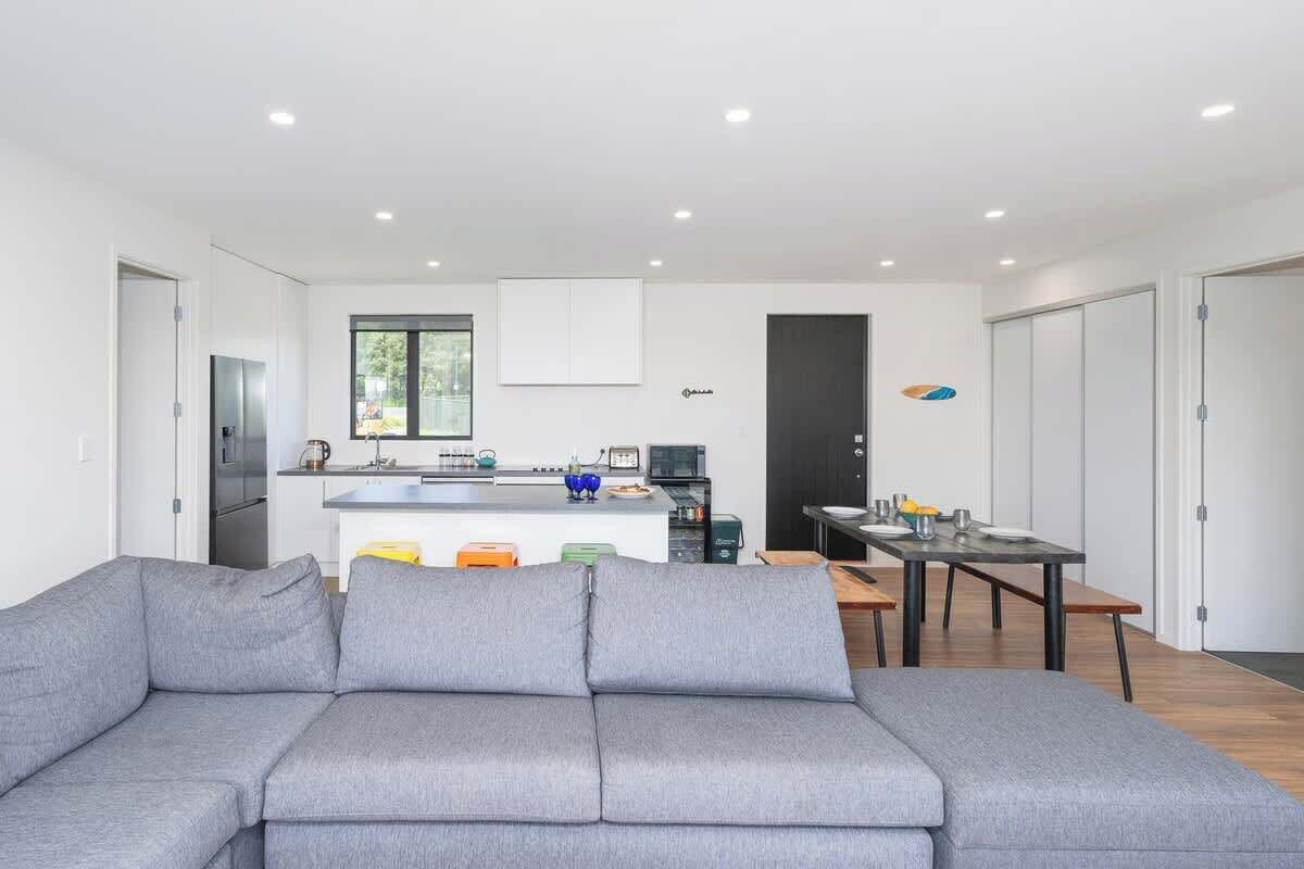 Un salon moderne avec un canapé gris, un coin repas comprenant une table et des chaises, et une cuisine en arrière-plan.