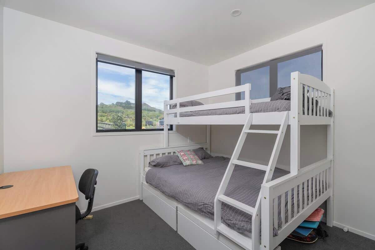 Habitación con literas, escritorio, silla, ventanas amplias y vista a la vegetación.