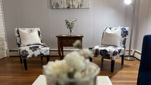 Ein Zimmer mit zwei stufenartigen Sesseln mit Blumenmuster, einem kleinen Holznachttisch mit Blumenvase und einem weißen Tisch im Vordergrund.