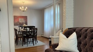 Ein gemütliches Wohnzimmer mit einem braunen Sofa, einem Esstisch mit Stühlen, einer Chandelier und einer weißen Ziegelwand.