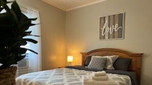 Ein ordentlich bezogenes Bett mit einem gemusterten Überwurf, einer Nachttischlampe und einem Schild mit der Aufschrift 'love'.