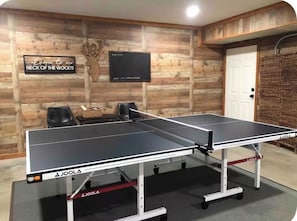 A ping pong table in a room with wooden walls, a mounted television, and a door. - Fall River Homestead Duplex A- 3BR- Near RMNP and Town (Estes Park)