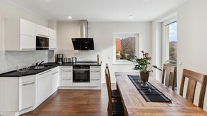 Una cocina moderna con armarios blancos, una estufa negra y un comedor con mesa y sillas de madera.