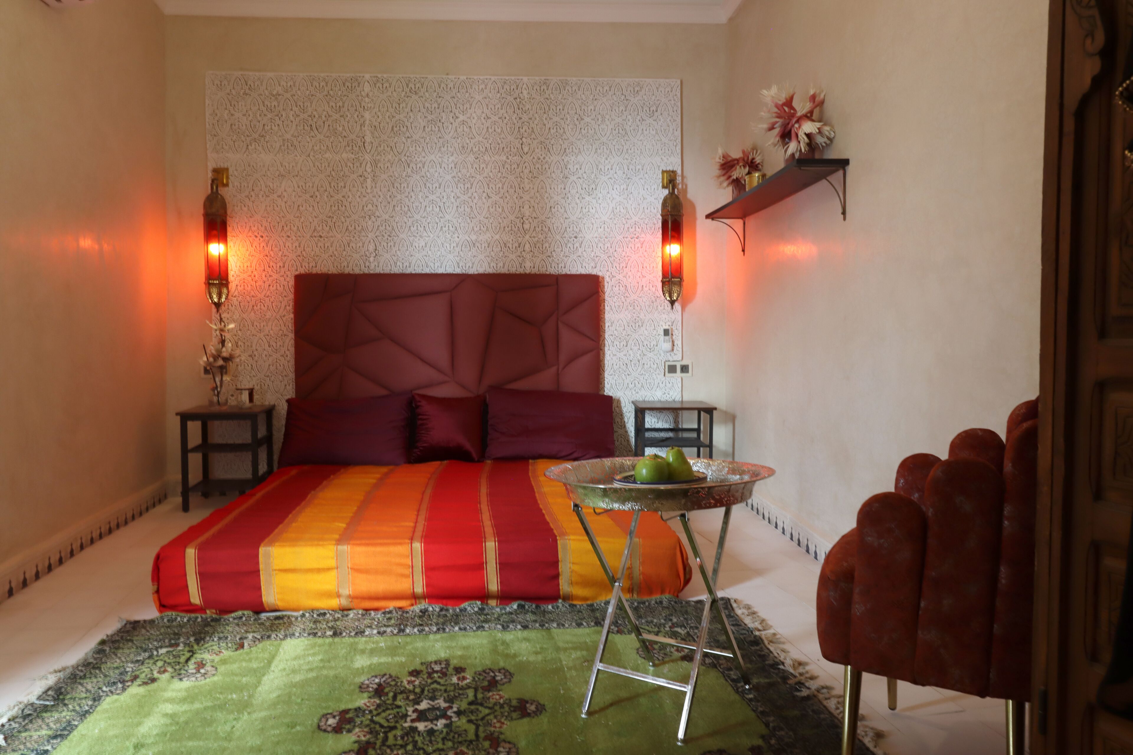 A bedroom with a large bed, a small round table with a glass top, and two wall-mounted lamps.