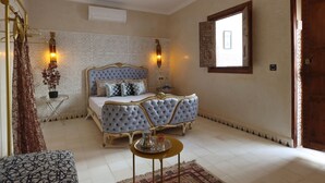 A bedroom with a large bed, a bedside table, a small round table, and a decorative mirror. - Riad la fayette bed & breakfast  (Marrakech)