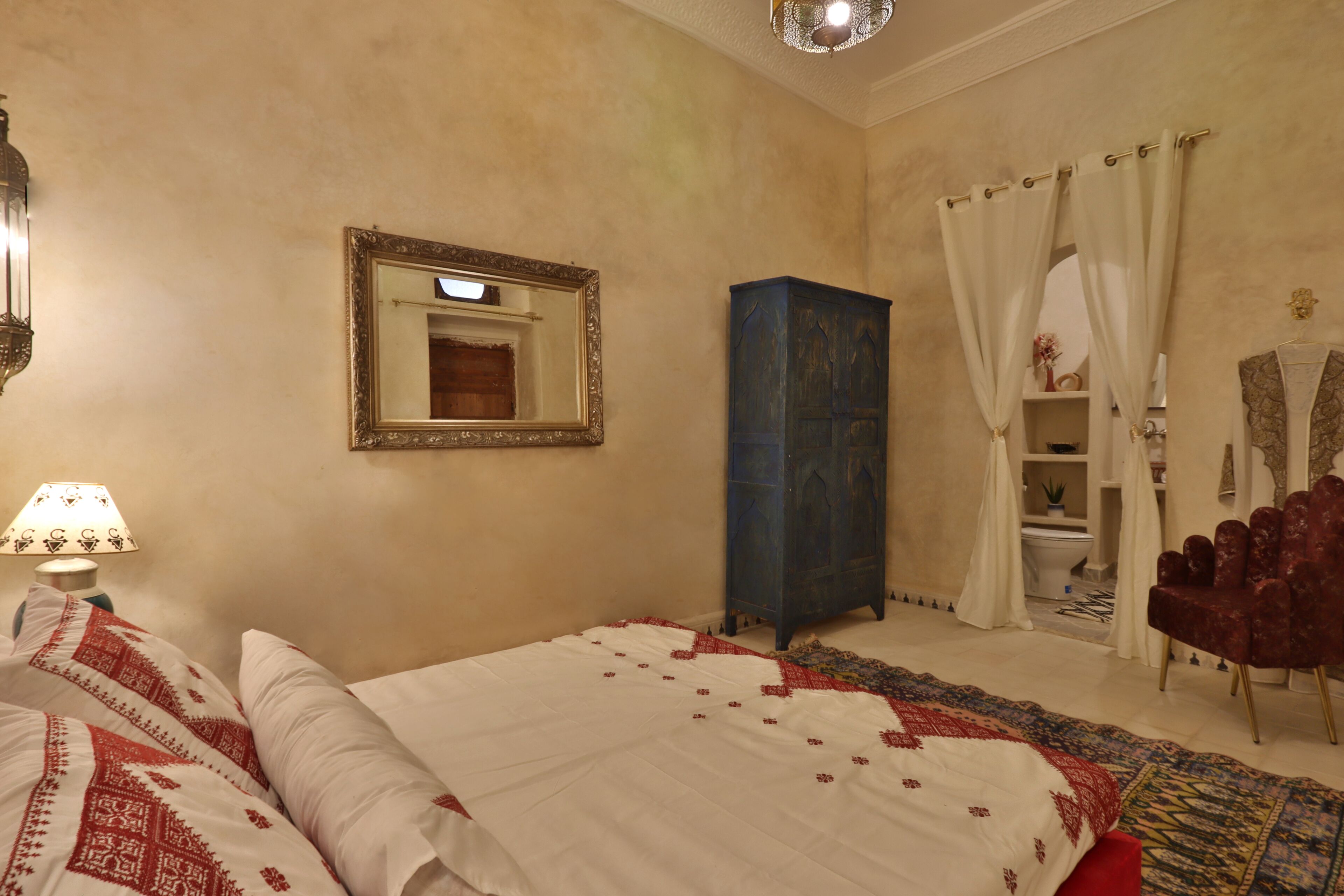Quarto com cama, guarda-roupa, cadeira, espelho e abajur.
