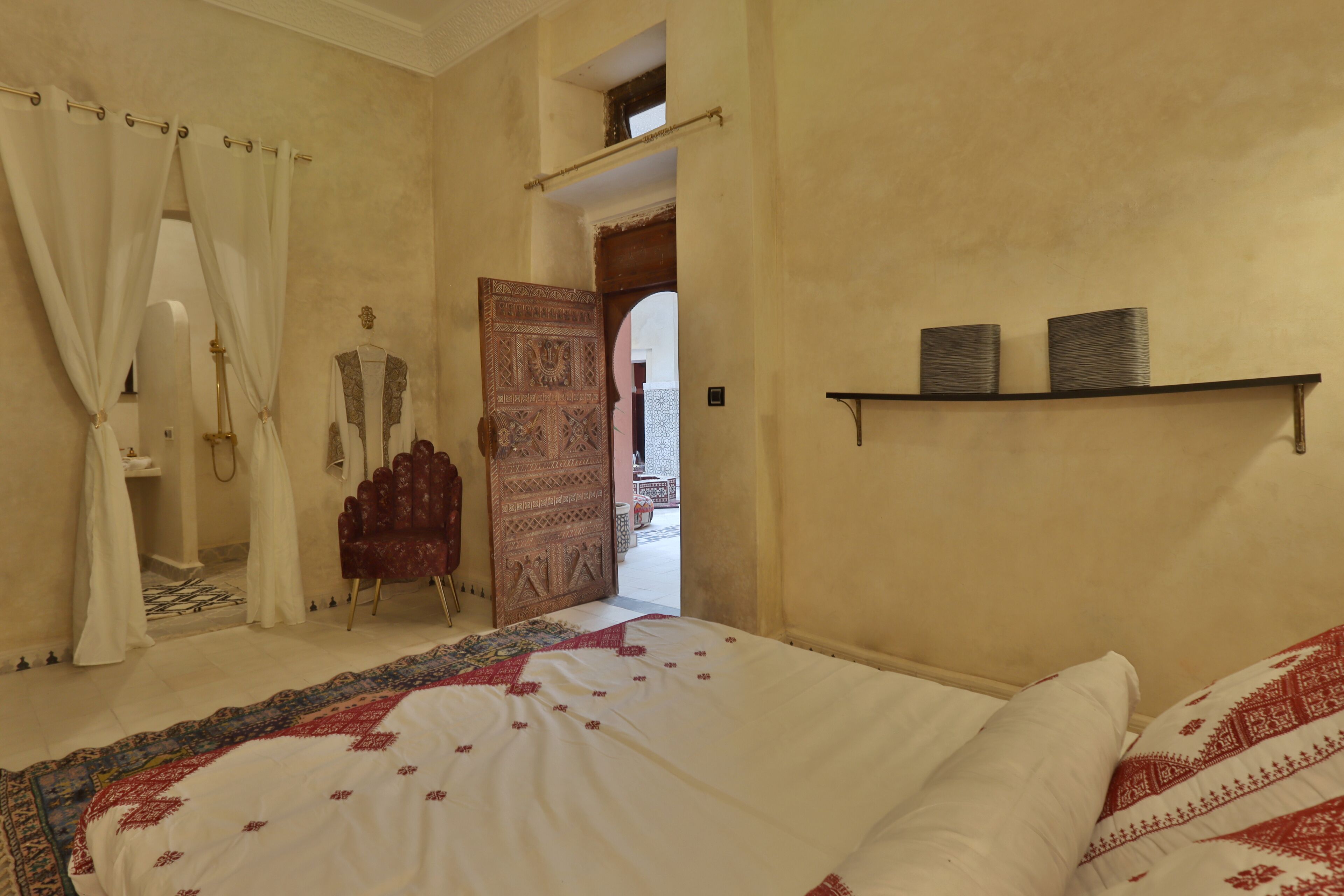 Una camera da letto con un letto grande, una sedia rossa, un tappeto decorato e una porta che dà su un'altra stanza.
