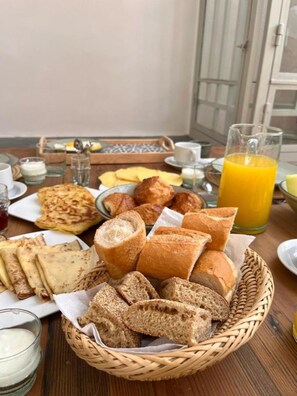 A breakfast table with various breads, pastries, and a glass of orange juice. - Riad la fayette bed & breakfast  (Marrakech)