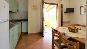 Una cocina con gabinetes verdes, un comedor con una mesa lista para dos personas y un televisor en la pared.