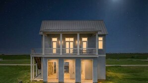 A two-story house with a balcony, a front door, and a staircase leading to the entrance. - Modern Beach Home with Stunning West Bay Views (Galveston)