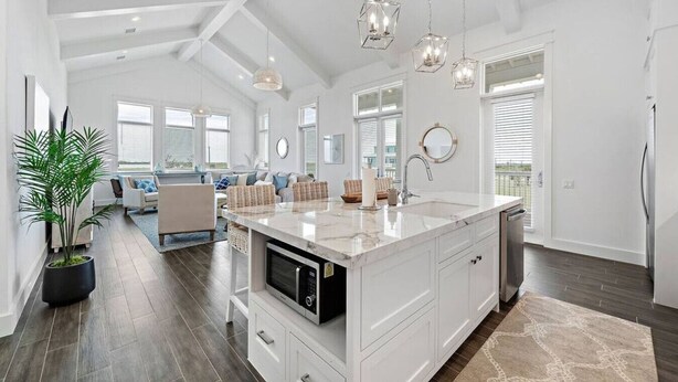 A spacious kitchen with a large island, modern pendant lights, and a view to the living area. - Modern Beach Home with Stunning West Bay Views (Galveston)