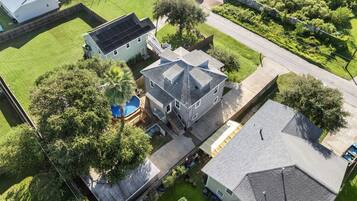 An aerial view of a residential area with a large house featuring a sloped roof, a visible garage, and a swimming pool.