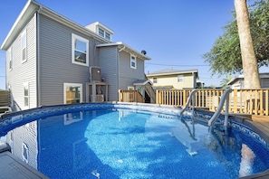 Une piscine avec une terrasse en bois et une maison en arrière-plan.