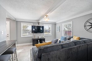 Un salón con un sofá gris, un televisor y una zona de comedor con mesa y sillas.