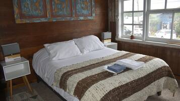 Une chambre avec un grand lit, deux tables de chevet, une fenêtre donnant sur des voitures garées et un mur orné d’œuvres d’art abstraites.