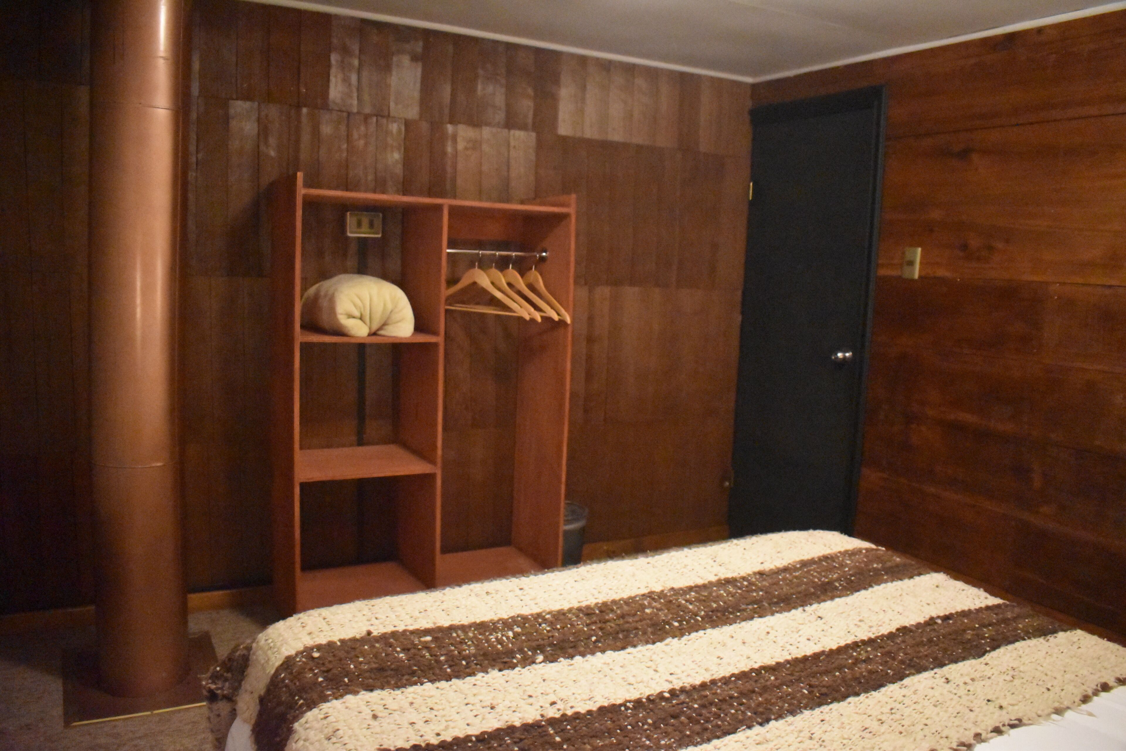 Un dormitorio con un armario de madera, una cama con manta a rayas y una puerta oscura.