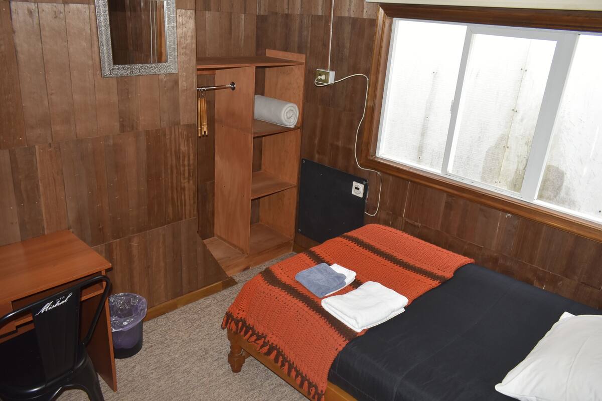 A wooden room with a bed, a desk, a wardrobe, and a window.