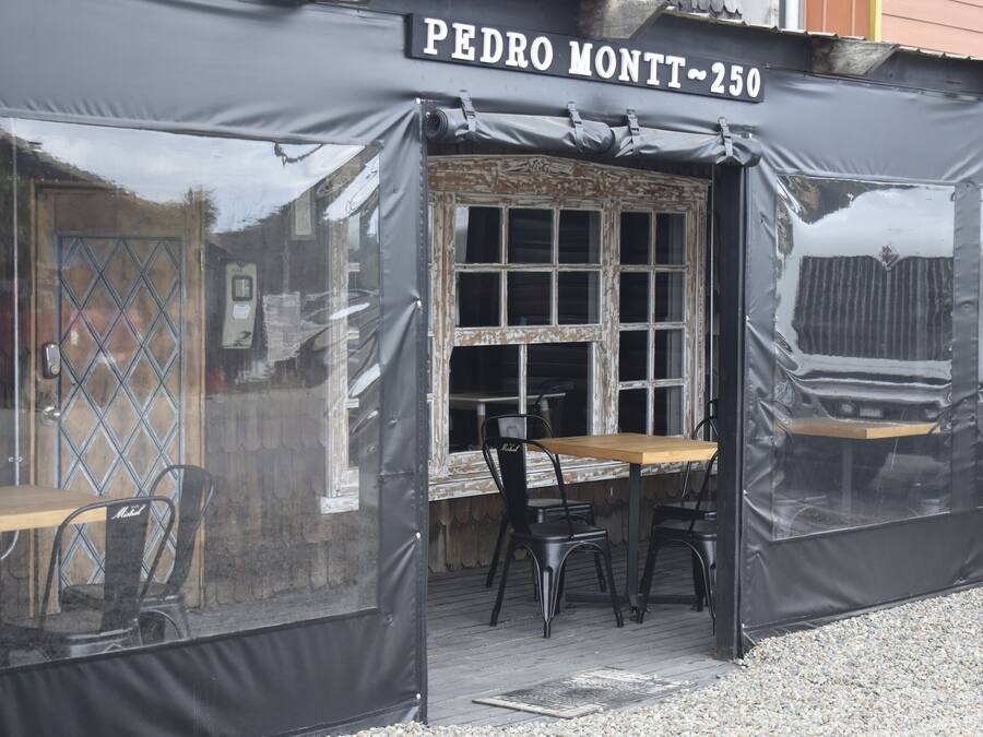 Un área de estar al aire libre cubierta con una mesa y sillas, una ventana con diseño de cuadrícula y un letrero que dice "PEDRO MONTT ~250".