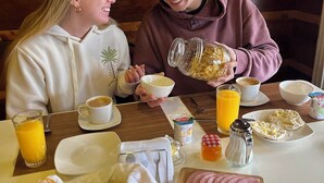 Un desayuno con una mesa de madera, platos, tazas y diversos alimentos como pan, queso y fruta.