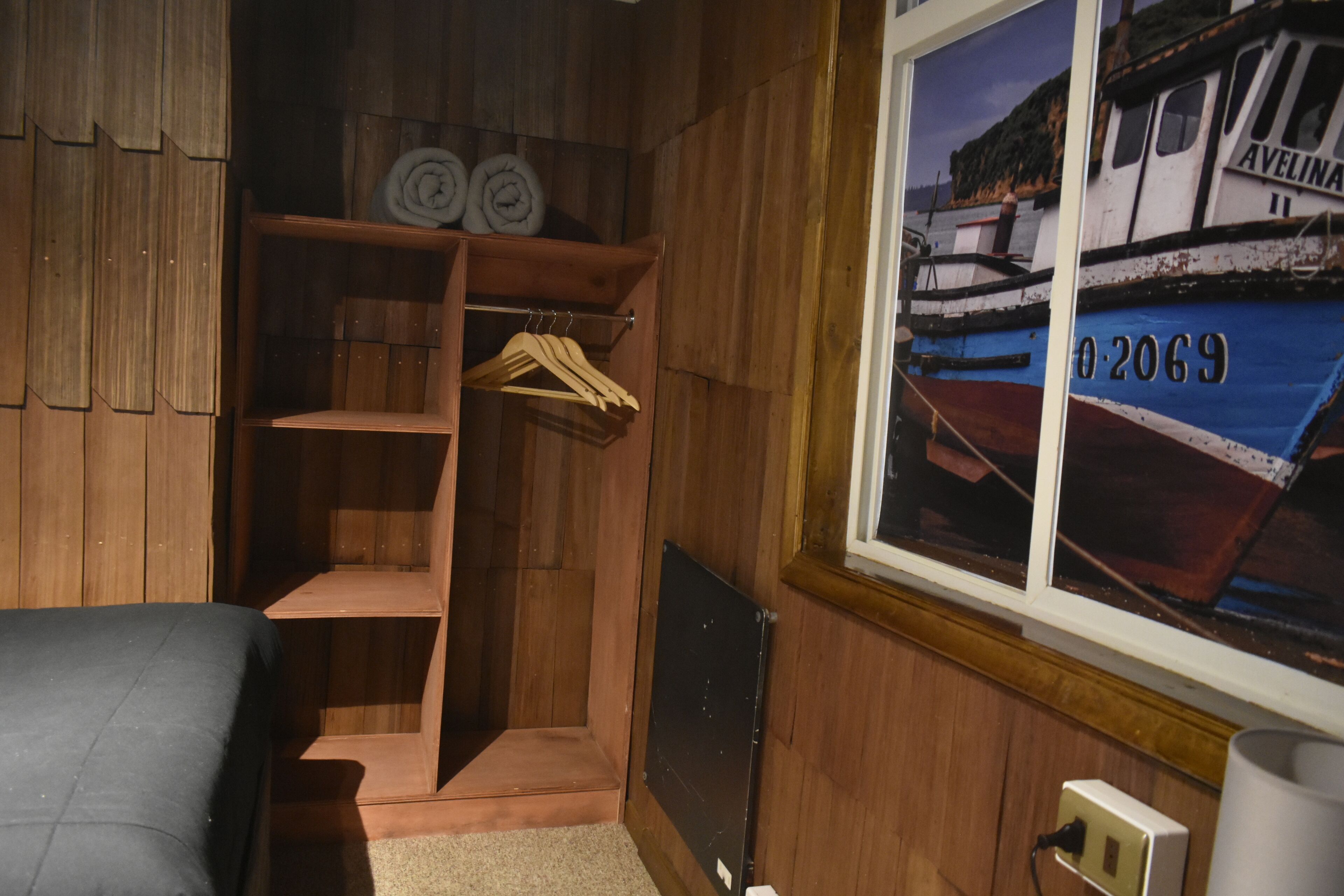Una habitación de madera con una cama, un armario de madera, una ventana con vista a barcos y un radiador.