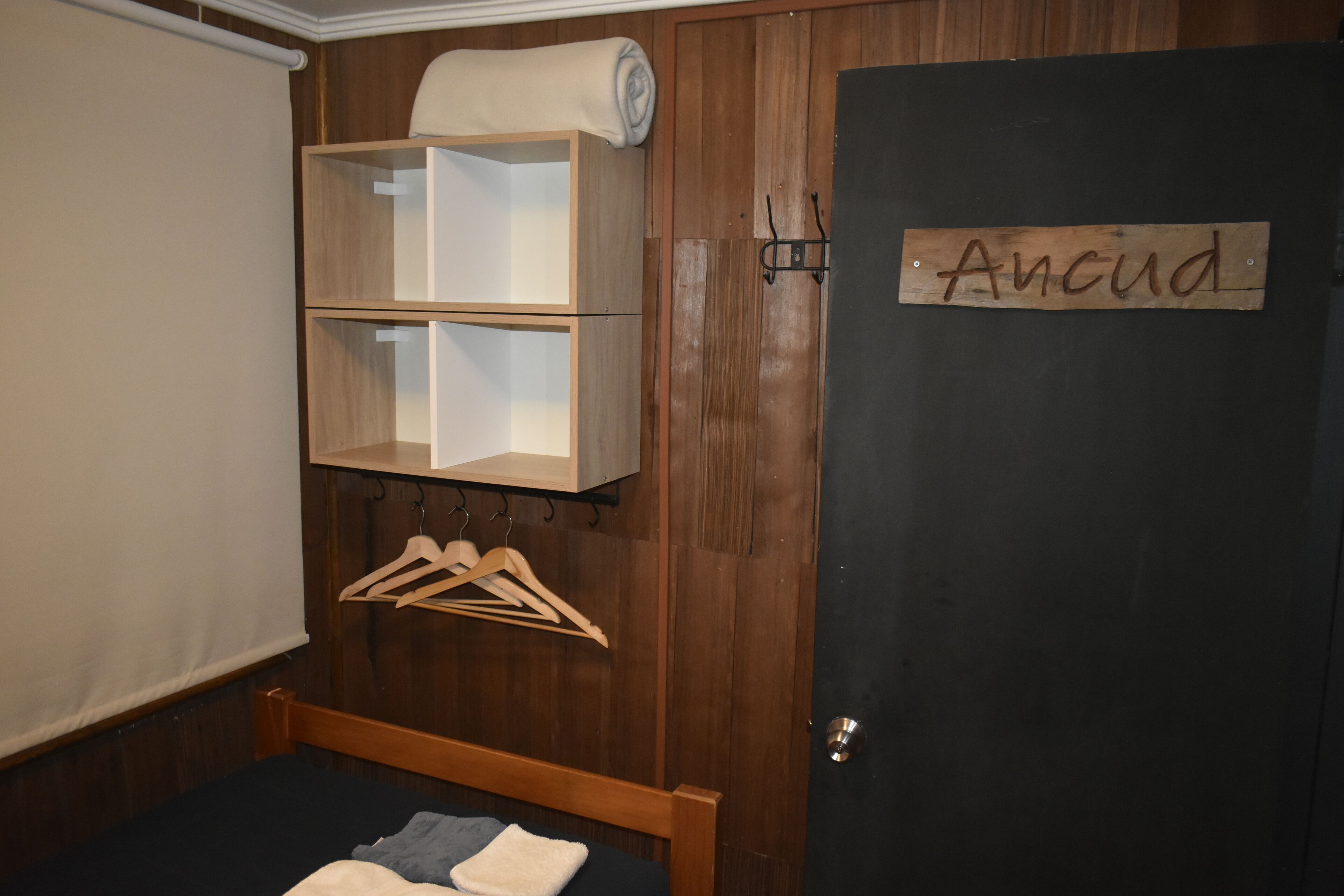 Een slaapkamer met een houten garderobe, een bed met een zwart matras, en een deur met de tekst 'Ancud'.