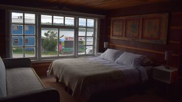 Un dormitorio con una cama grande, una silla, una mesita de noche y una ventana con vistas a un muelle y barcos.