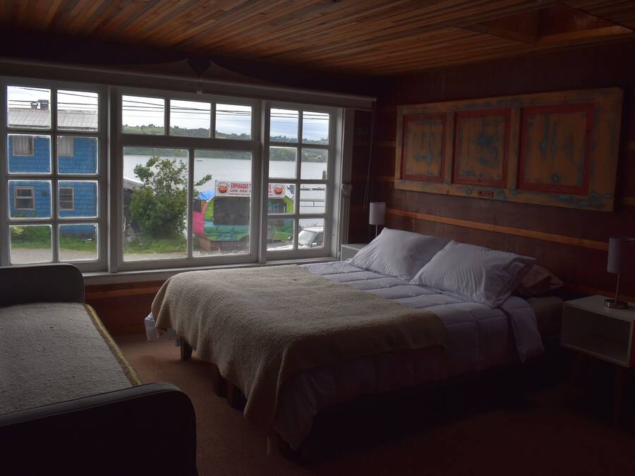 Un dormitorio con una cama grande, una silla, una mesita de noche y una ventana con vistas a un muelle y barcos.