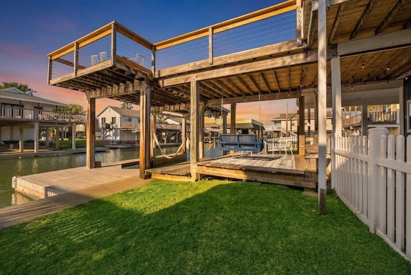 A wooden deck with a pool, surrounded by a white fence and a grassy area.