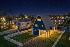 A house with a blue exterior, a garage, and a fenced yard at night.