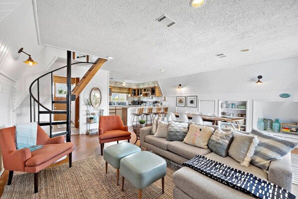 A spacious living area with a curved staircase, a kitchen in the background, and a dining area.