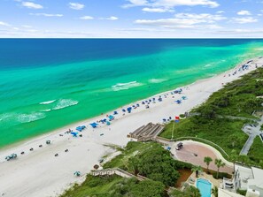 A beach with clear turquoise waters, a sandy shore, and a pool area with a wooden deck. - Seagrove- 3 Min walk to Beach, 2 BR, Pool, Tennis & sleeps 6 (Santa Rosa Beach)