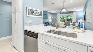A modern kitchen with a dishwasher, white cabinets, a sink, and a dining area with a table and chairs. - Cassine- 3 Min to Beach, 2 BR, Pool, Bikes, Tennis & Beach (Santa Rosa Beach)