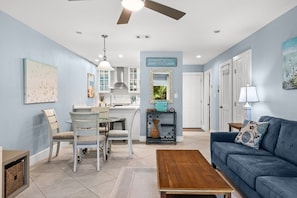 A living room with a blue sofa, a coffee table, and a dining area with chairs and a table. - Seagrove- 3 Min walk to Beach, 2 BR, Pool, Tennis & sleeps 6 (Santa Rosa Beach)