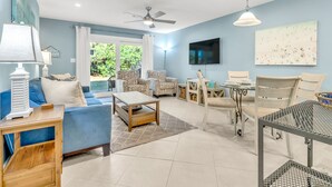A spacious living room with a blue sofa, patterned armchairs, a coffee table, and a dining area with chairs and a table. - Cassine- 3 Min to Beach, 2 BR, Pool, Bikes, Tennis & Beach (Santa Rosa Beach)