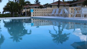 Une piscine aux eaux cristallines, bordée de carreaux, agrémentée de palmiers et de chaises longues.