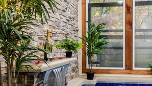 Un mur de pierres avec une petite cascade, un bassin et des plantes en pot.