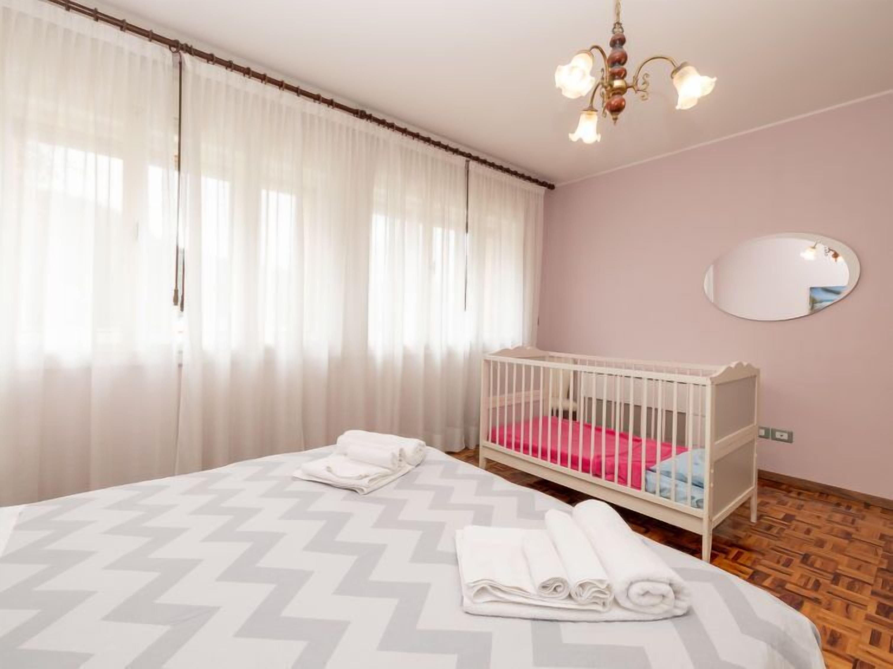 A bedroom with a bed, a crib, a mirror, and a chandelier.